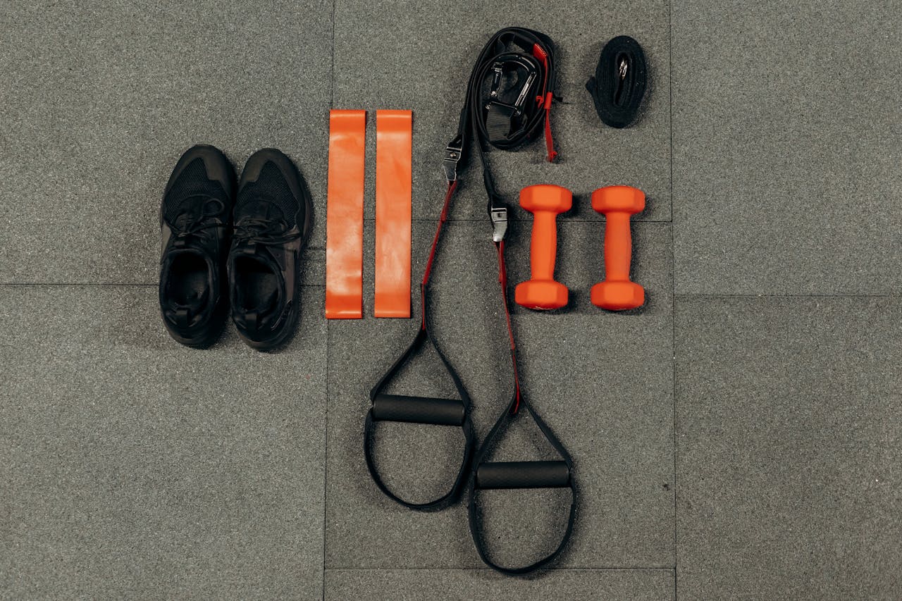 hero-img-01 Flat lay of fitness gear including dumbbells, sneakers, and resistance bands for a home workout.